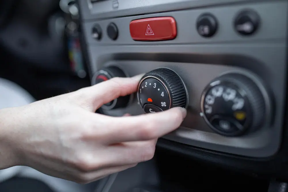 A person's hand turning the fan speed dial on a car dashboard for car ac repair diagnostics.