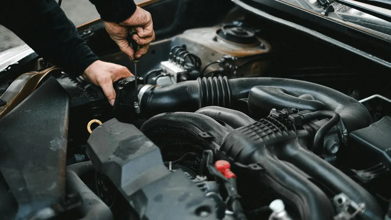 Mechanic using a screwdriver to tighten engine hose during a starter motor repair.