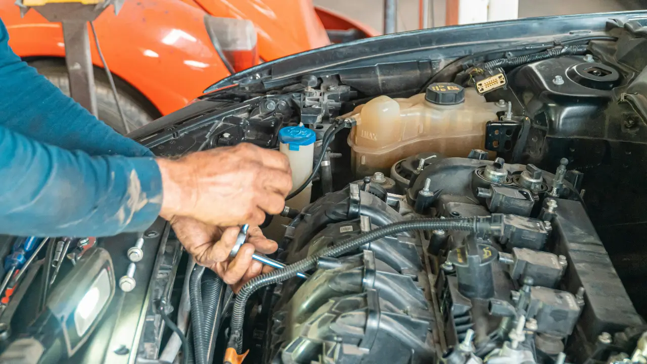 Mechanic using a wrench for a starter motor repair on a car engine.