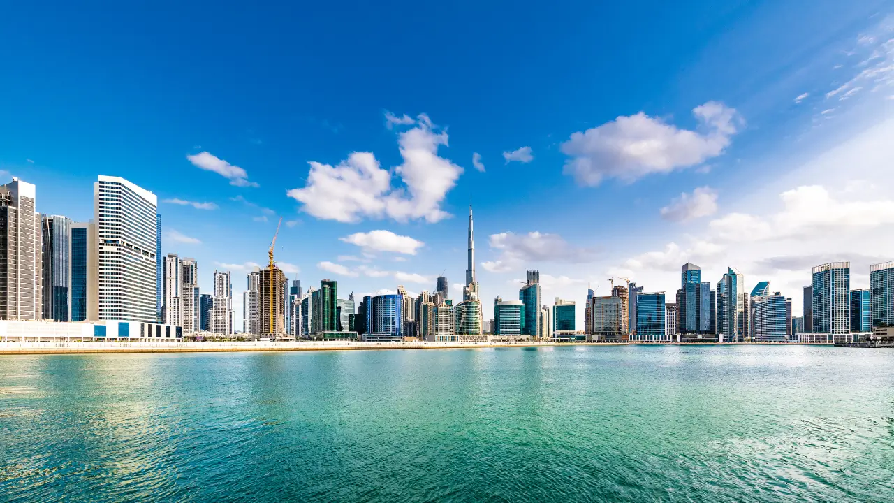 Panoramic view of the Dubai skyline with skyscrapers and the Burj Khalifa over the water.