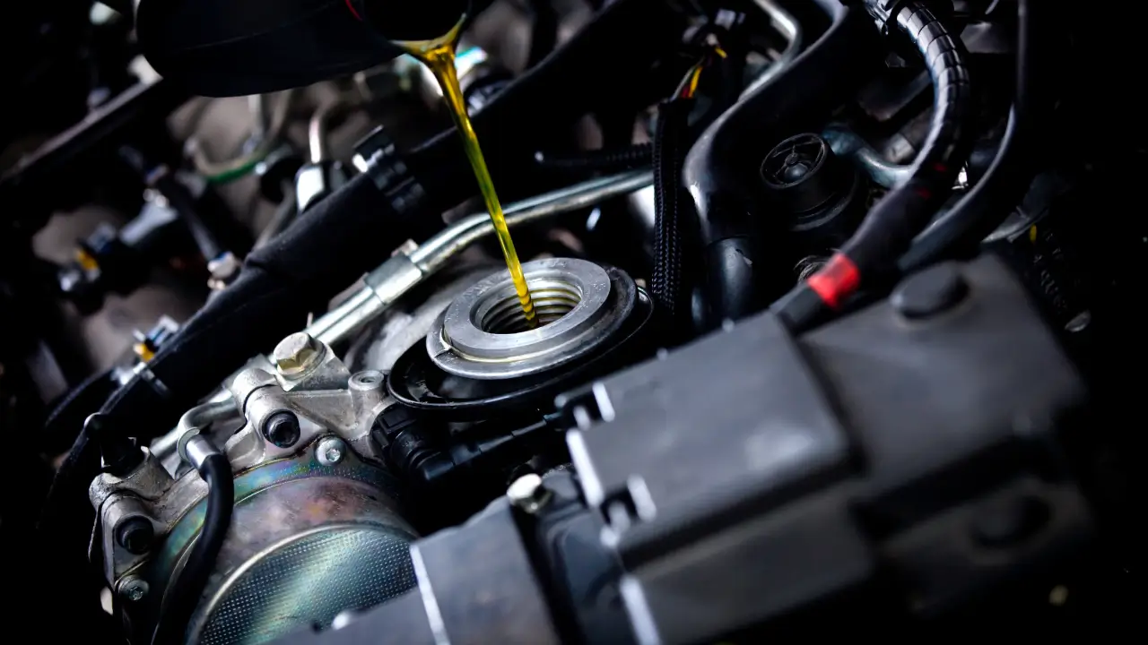 Close-up of golden synthetic motor oil pouring directly into an open car engine oil filler neck