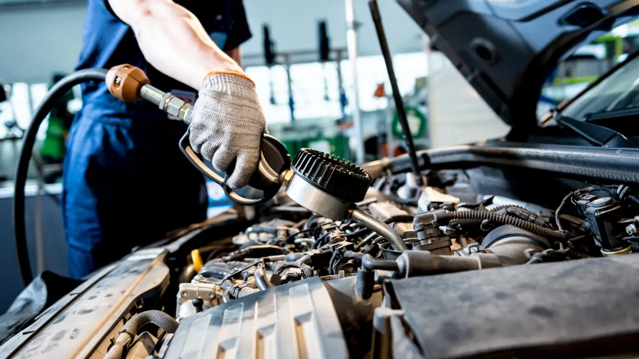 Mechanic holding pressure gauge to refill car air conditioning refrigerant gas in open engine bay